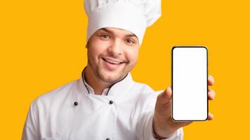 Food Delivery App. Chef Man Showing Phone With Blank Screen Recommending Catering Service Standing On Yellow Studio Background. Panorama photo