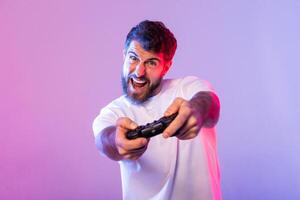 A bearded man intently plays games, gripping a controller and showing an excited expression, illuminated by vibrant pink and blue studio lighting. photo