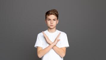 Teenager with arms crossed in an X shape, showcasing refusal or denial, isolated on a grey background photo