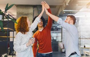 Happy coworkers having fun, giving high five during friendly talk in office, coffee break. photo