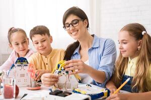 A teacher is assisting a group of students as they build robot models during a STEM classroom lesson. The students appear engaged and excited as they work on their projects photo