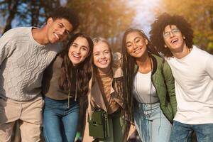 Group portrait of happy multiracial teenaged friends spending time together in autumn park photo
