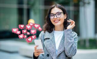 This image shows a woman in a grey blazer, holding a smartphone in her hand. She is smiling and looking at the device. There are several heart-shaped icons floating above her phone photo