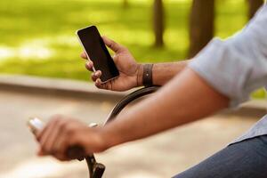 Ride Navigation. Unrecognizable afro man riding bike and holding smartphone with black screen, using online maps app, cropped image, closeup photo