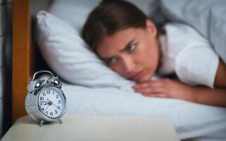 Sleep Disorder. Young Woman Looking At Clock Lying In Bed Suffering From Insomnia At Home. Selecive Focus photo