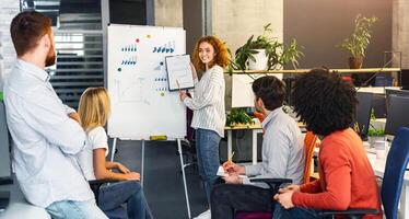 A confident young woman stands presenting a chart to a group of attentive colleagues during a collaborative meeting in a contemporary workspace photo