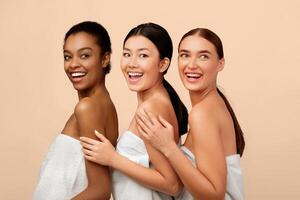 Three Happy Diverse Women Posing In Bath Towels Standing Over White Background. Studio Shot photo