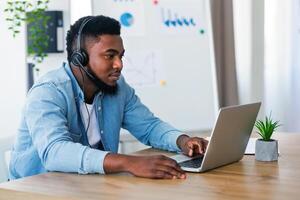Young call center operator in headset solving issues with client online, using laptop at workplace in office photo