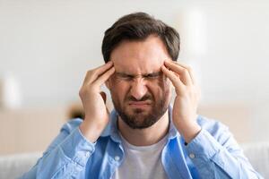 A man is holding his head with his hands, showing signs of stress or distress. He appears overwhelmed or in deep thought, with a facial expression reflecting his inner turmoil. photo