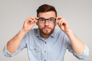 Young man showing his big eyes in glasses and trying to see something, isolated on grey studio background photo