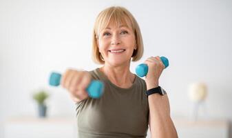 Home training concept. Strong senior woman doing exercises with dumbbells indoors. Cheerful mature lady working out her arm muscles, keeping fit, leading healthy lifestyle during covid-19 isolation photo