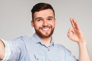 Handsome guy showing OK sign and making selfie against studio background, panorama photo