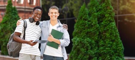 College Mates. Two multiethnic male students posing outdoors after classes, standing over university background, embracing and smiling at camera photo