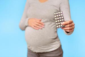 Unrecognizable Pregnant Girl Showing Pills Blister Pack Standing Over Gray Background In Studio. Selective Focus, Cropped photo