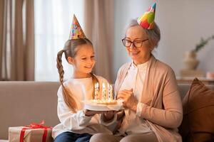 An older woman and a young girl sit on a couch, smiling at a birthday cake in front of them. The woman is lighting candles on the cake while the girl eagerly awaits a slice. photo