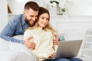 A man and woman are seated on a couch, both looking attentively at a laptop screen placed in front of them. photo