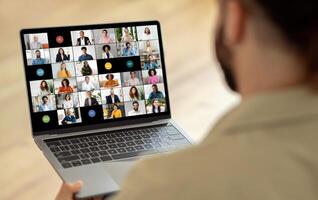 A man is seated in front of a laptop, where a screen displays a call with multiple people. He appears focused and engaged as he interacts with the group virtually. photo