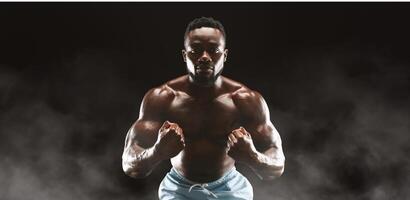 A muscular man with a determined expression poses against a dark background with smoke swirling around him. photo