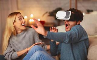 Excited Couple Using Virtual Reality Headset Having Fun Experiencing VR At Home In The Evening. photo