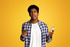 Enjoy Song. African-American Guy Listening Music on Smartphone Online, Yellow Background photo
