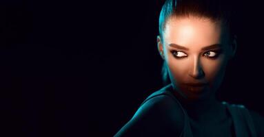 A woman is standing in the dark, her eyes fixed at copy space, with a somber expression on her face. The darkness around her adds an eerie atmosphere to the scene, panorama photo