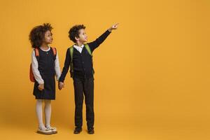 African American young boy and a girl schoolers are pointing at an indiscernible object or direction on yellow background. Their fingers are extended and they are looking intently at the same point. photo