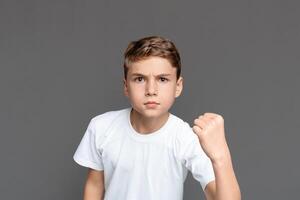 This image captures a teenager clenching his fist in determination or defiance, with a focused look, isolated against a grey backdrop photo