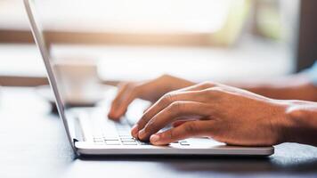 A guy is sitting at a desk, focused on typing on a laptop computer. The screen displays various applications. He appears to be working or communicating online. photo