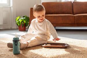 A young boy is seated on the floor, engrossed in playing with a tablet device. His focus is on the screen as he interacts with the digital content photo