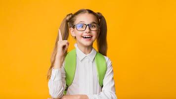Idea Concept. Excited Primary School Girl Pointing Finger Up Over Yellow Studio Background. Empty Space photo