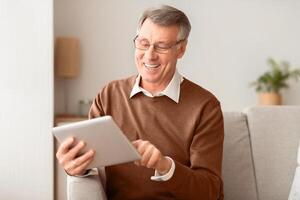 Gadget Lifestyle. Senior Man With Tablet Computer Browsing Internet Reading News Sitting On Sofa At Home. Selective Focus photo