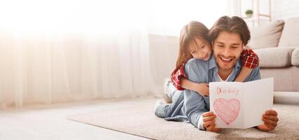 Happy father reading greeting self-made card while bonding with daughter on floor at home, free space photo