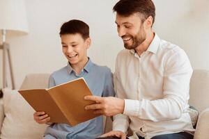 Happy Boy And Loving Dad Reading Book Sitting Together On Sofa At Home. Father And Son Relationship. Selective Focus photo
