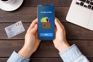 Mobile banking. Woman holding smartphone with digital wallet application. credit card on table, top view photo