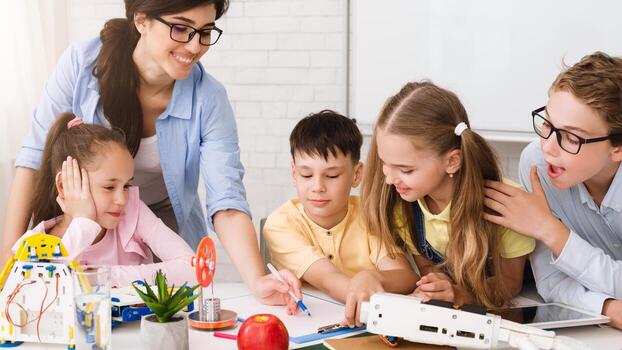 A group of elementary school students are engaged in a STEM learning activity in a classroom setting. They are working with robots and building models, and a teacher is guiding their learning photo