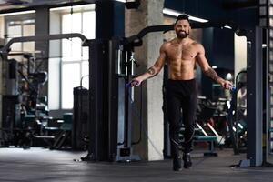 A shirtless man with tattoos is jumping rope in a gym. He is smiling and appears to be enjoying his workout. photo
