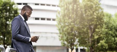 Attractive happy businessman is texting on cell phone near modern office building, side view with copy space. Business, technology and communication concept photo