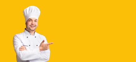Look There. Male Chef Pointing Fingers Aside Standing On Yellow Studio Background. Panorama, Free Space For Text photo
