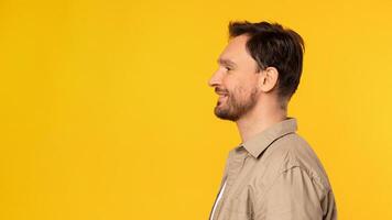 A man is standing upright in front of a bright yellow background. He is positioned centrally in the frame and is wearing casual attire, side view photo