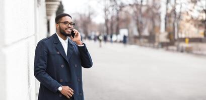 African American man in formal outfit have phone conversation outdoors, standing by modern building on the street, panorama with copy space photo