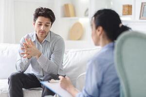 Unhappy man sitting on a couch engaged in conversation with a therapist in a office setting. The man appears focused and attentive while the therapist listens and provides guidance. photo