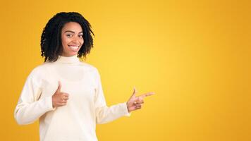 Look There. Happy afro woman pointing index finger at copy space, showing thumb up over yellow studio background photo