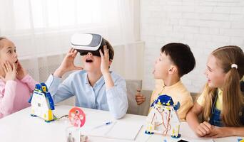 A group of children are engaged in a STEM learning activity, building robots and exploring virtual reality. One child wears a VR headset and looks amazed at the experience photo