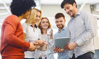 A diverse group of individuals standing side by side, looking attentively at a tablet device in the center. They appear engaged, possibly discussing or collaborating on the digital content displayed. photo