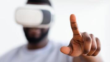 A close-up photo shows African American man wearing a virtual reality headset, his right hand extended forward, with his index finger pointing up as he interacts with digital content.