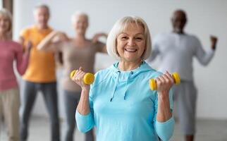 Multiracial group of senior people in sportswear doing strength building fitness exercises with dumbbells, holding fitness tools and smiling at camera, selective focus on positive elderly lady photo