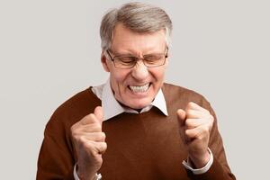 Anger. Angry Elderly Man Clenching Fists And Frowning Posing On Gray Background. Studio Shot photo