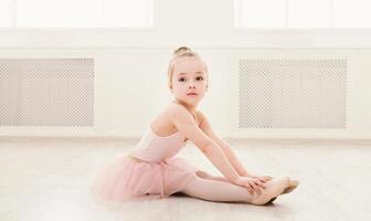 Portrait of little ballerina on floor, copy space. Smiling baby girl dreaming to become professional ballet dancer, classical dance school photo