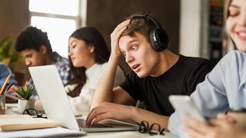 Shocked student guy looking test results on laptop, studying with classmates in library photo