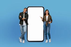 With joyful faces, the young multiethnic man and woman pose beside a blank-screened, life-sized smartphone, emphasizing the endless possibilities for customization. photo